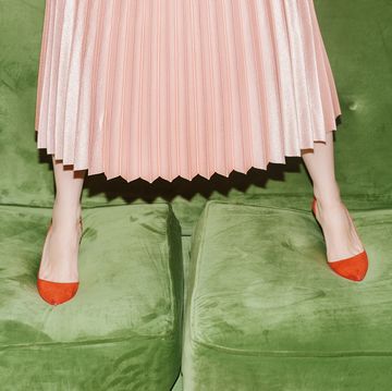woman with pleated skirt standing on green velvet sofa